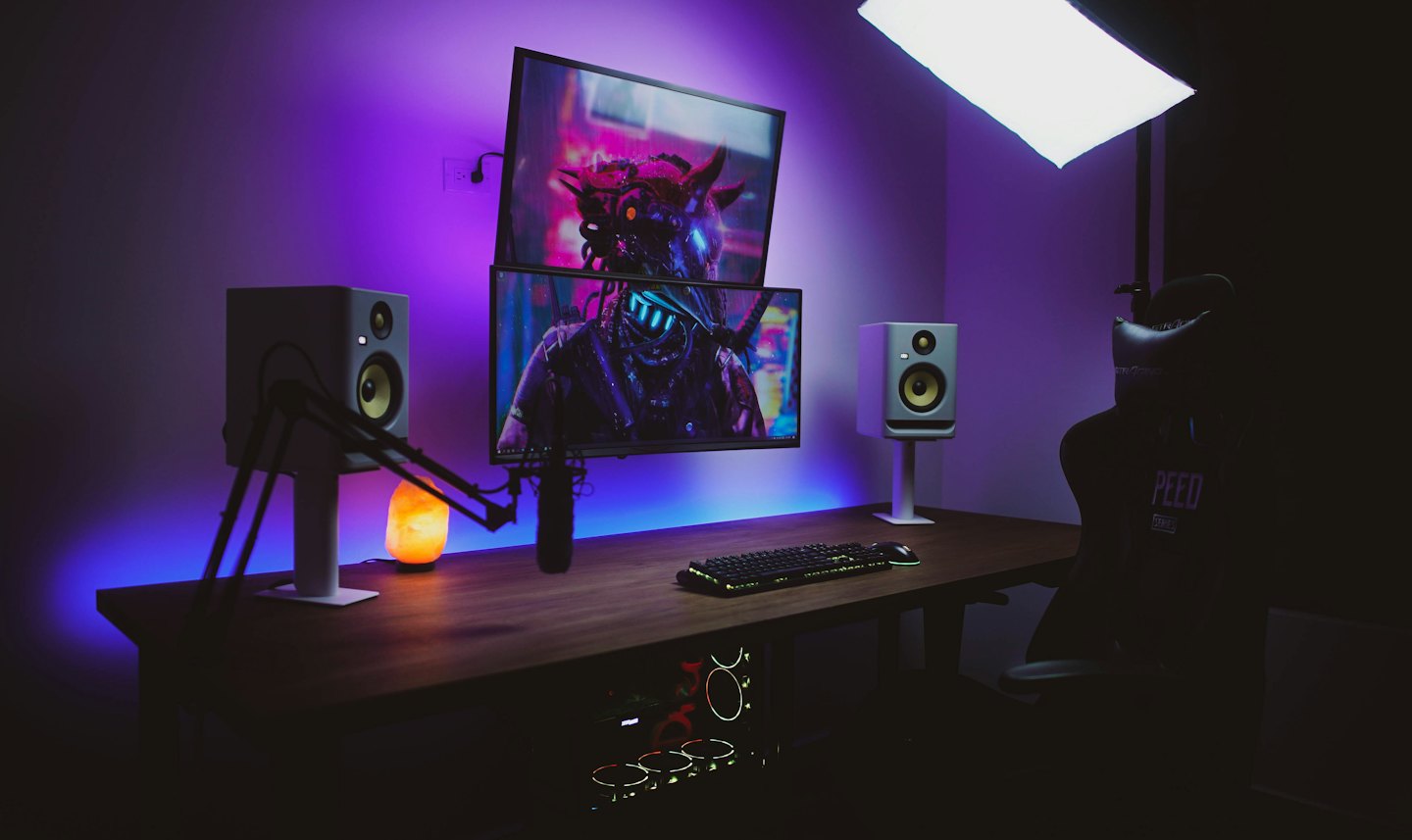 Gaming-Setup mit gestapelten Monitoren und Mikrofon auf einem Schreibtisch.